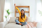 Fototapeta  - Happy young asian woman relax on comfortable couch at home texting messaging on smartphone, smiling girl use cellphone, chatting online message, shopping online from home