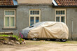 Covered car on a yard . The car is covered with a cover.