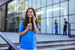 A cheerful female nurse smiles as she talks on her smartphone as she walks to work in a city medical building. After work. Nurse Using Her Mobile Phone While Taking a Break.