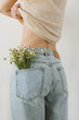 Backside view of young pretty woman. Chamomile flowers bouquet in jeans pocket