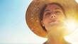 A woman wearing a straw hat is smiling and looking up at the sun
