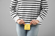 Cystitis. Woman holding sticky note with drawn sad face on grey background, closeup