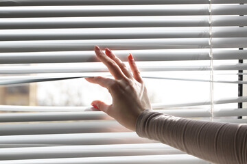 Woman separating slats of white blinds indoors, closeup