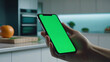 hand holding smartphone with blank green screen in modern kitchen setting, perfect for showcasing cooking apps or home management software. blurred background of kitchen, culinary app demonstrations