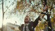A man in a suit jubilantly throws money into the air amidst autumn trees.