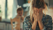 Stressed mother hiding face while her child's figure is blurred in the background.