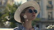 Stylish woman in sunglasses and sunhat, embracing urban summer vibes.