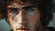Intense gaze of a young man with curly hair and striking blue eyes.