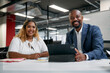 Two multiracial business people looking at camera and smiling while using digital tablet in office
