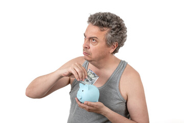 Wall Mural - A gray-haired, shaggy, unshaven middle-aged man in a sleeveless T-shirt holds a piggy bank and a 100 US dollar bill in his hands.