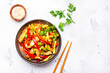 Stir fry turkey breast with red paprika and zucchini with sesame seeds, lime, garlic, ginger and soy sauce in ceramic bowl. White table background, top view