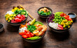Poke bowls for balanced diet with vegetables, legumes, seafood, avocado and rice, wood table background, top view