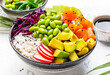 Poke bowl for balanced nutrition with salmon, avocado, radish, cabbage, edamame beans and rice, white table background, top view