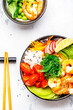 Balanced dier. Poke bowl with shrimp, rice, avocado, vegetables and chuka salad, white table background, top view