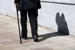Old woman walking with a cane down the city street. Diseases of the spine and legs of elderly people