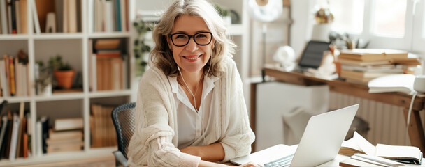 Wall Mural - A mature woman with glasses sits at a desk, focused on her laptop screen in a home setting.