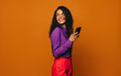 Cheerful woman using vibrant mobile phone against orange background