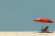 A beach scene with a red umbrella and a chair