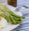 Cooked green asparagus stalks and sprinkled with grated cheese in a white plate