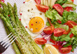 Round plate with cooked asparagus, fried egg, avocado and fresh vegetable salad on the table
