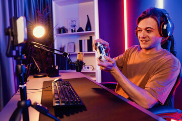 Enjoy smart gaming streamer with control joystick, playing game online of live streaming by smartphone rec with team skilled players on computer at modern technology cyber neon light room. Pecuniary.