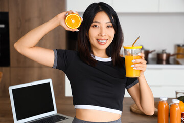 Poster - Sporty Asian woman with orange and glass of juice in kitchen