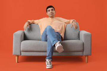 Poster - Handsome young man sitting on grey sofa against orange background