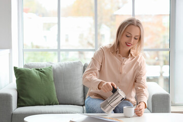 Poster - Pretty young woman pouring espresso from geyser coffee maker into cup in living room