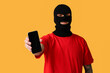 © Pixel-Shot - Handsome young man in balaclava with mobile phone on yellow background