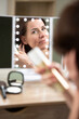 woman spraying hairspray reflected in illuminated mirror