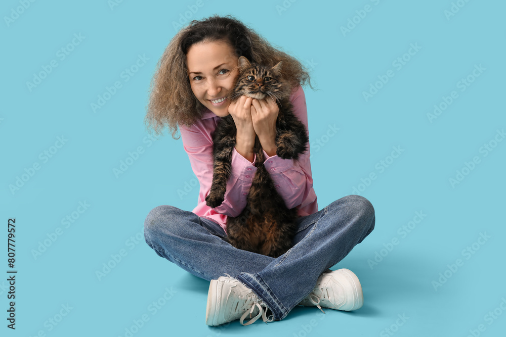 Mature woman with cute cat sitting on blue background