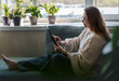 Caucasian mature middle aged woman wearing glasses sitting on the couch at home using a tablet