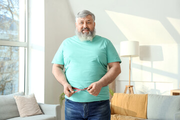 Canvas Print - Overweight happy mature man with measuring tape at home. Weight loss concept