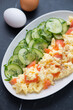 Scrambled eggs with smoked salmon and cucumber salad, vertical shot on a black marble background, middle close-up, selective focus