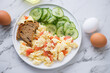 Scramble with smoked salmon, toasts and cucumber salad on a white marble background, horizontal shot, elevated view