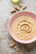 Roseate bowl with peanut butter or paste made from ground, dry-roasted peanuts, vertical shot on a beige granite background