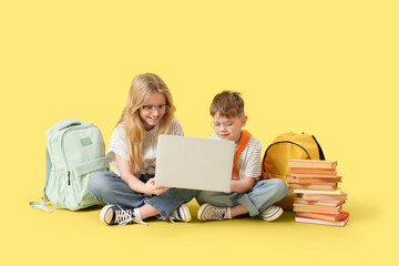 Wall Mural - Cute little pupils in eyeglasses using laptop on yellow background