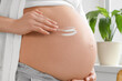 © Pixel-Shot - Young pregnant woman applying cream on her tummy at home, closeup