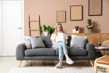 Canvas Print - Young woman sitting on sofa in stylish living room