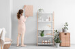 © Pixel-Shot - Young woman hanging picture near shelving unit in white room