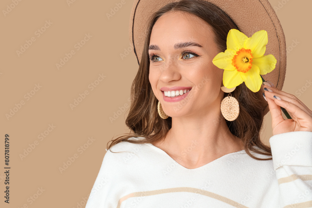 Beautiful young woman with daffodil on brown background, closeup