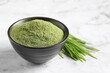 Wheat grass powder in bowl and fresh sprouts on white marble table, closeup