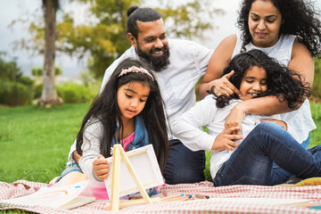 Wall Mural - happy indian family having fun painting with children outdoor at city park - spring time and parenth