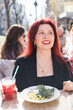 Millennial woman eating italian pasta at restaurant on the street in spring. Concept of Italian gastronomy and travel. Stylish woman with red hair