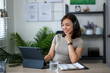 © Wasana - A woman wearing headphones is sitting at a desk with a laptop and a tablet. She is smiling and she is enjoying her work