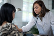 © Wasana - A woman doctor is examining a woman in a hospital room. The woman is wearing a white coat and the doctor is wearing a white coat. The doctor is using a stethoscope to listen to the woman's heartbeat