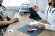 © Wasana - A woman is sitting at a desk with a doctor. The doctor is writing something on a piece of paper