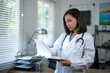 © Wasana - A woman in a white lab coat is looking at a piece of paper. She is a doctor and is reading the paper