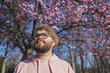 Man allergic enjoying after treatment from seasonal allergy at spring. Portrait of happy bearded man smiling in front of blossom tree at springtime. Spring blooming and allergy concept. Copy space