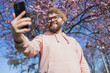 Happy curly man takes selfie against backdrop of flowering tree in spring for his internet communications. Weekend and social networks concept